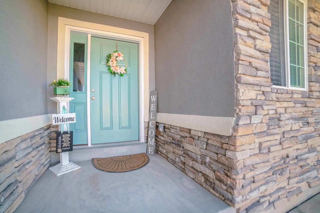 Teal front door with welcome sign and stone wall siding