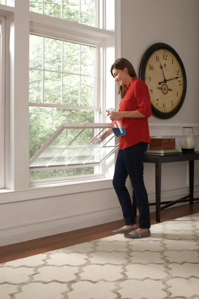 Woman cleaning double-hung tilt window in living room